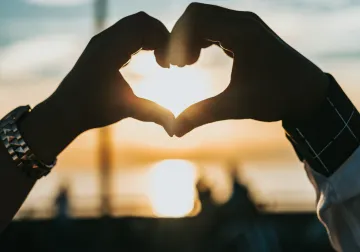 Dos manos forman un corazón frente a la luz del atardecer