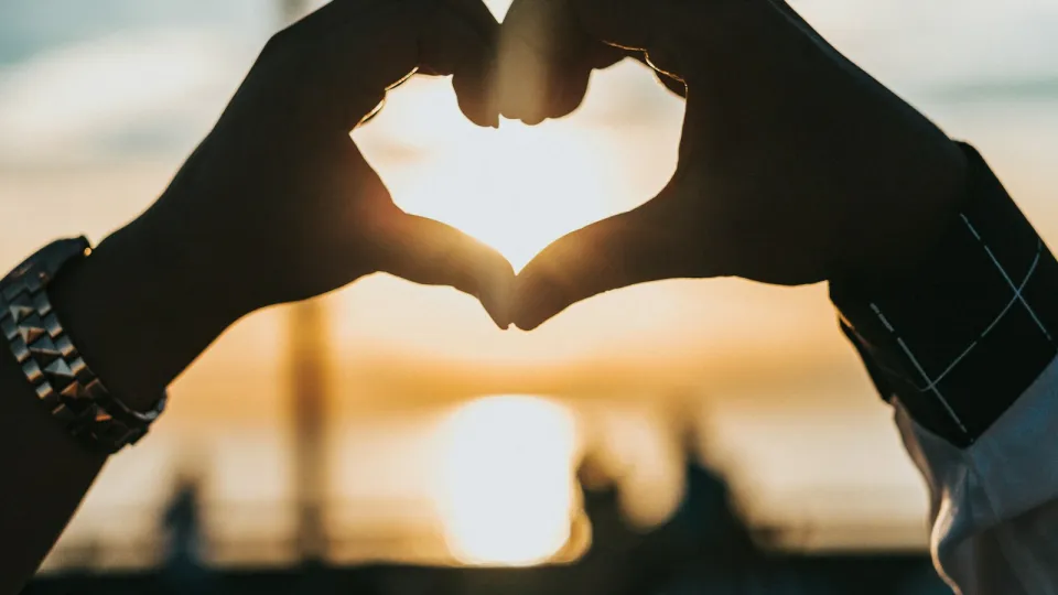 Dos manos forman un corazón frente a la luz del atardecer